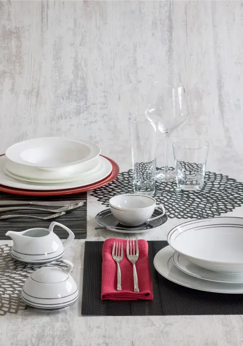 Platos pandos y hondo de porcelana blanca china, pertenecientes a la vajilla Spirale, de Fortessa; plato base de vidrio rojo ketchup, de la alemana Loveplay; cubiertos Bamboo por cinco piezas, de Sambonet; vajilla por cinco piezas, azucarera y jarra, Tac Dynamic, de Rosen Thal, diseño de Walter Gropius; vasos largo y corto Tossa, y copa Pure, de Schott; individuales redondos en negro y silver, e individuales Tuxedo en negro y gris/negro, ambos de Chilewich, todo lo anterior en Carmiña Villegas. Servilleta de lino color cereza, de Tabletop.