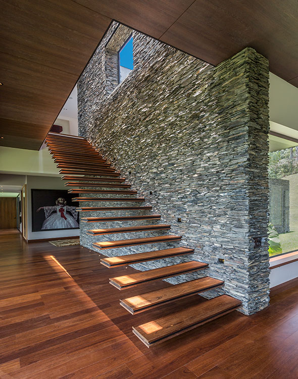 El muro revestido en piedra soporta los pasos en voladizo de la escalera que sube al estudio y a la habitación principal. Al fondo, una fotografía de Adriana Duque.